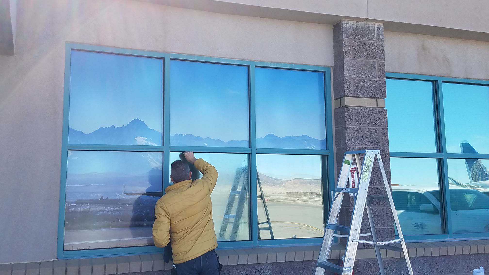 Professional installation of commercial window film with crisp mountain reflection